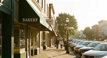 A neighbourhood main street lined with small local shops on a bright morning.